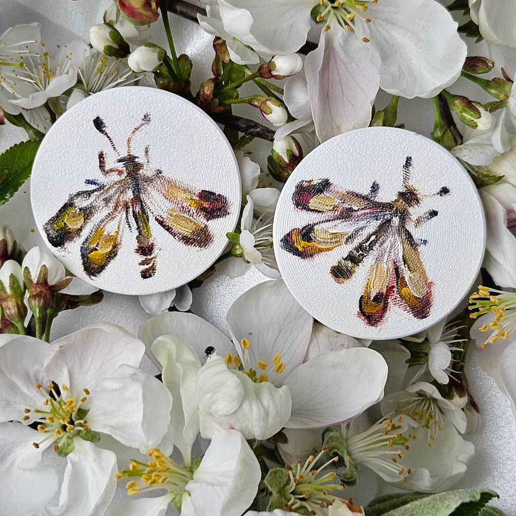Two oil painted colorful moths on earrings surrounded by white flowers.