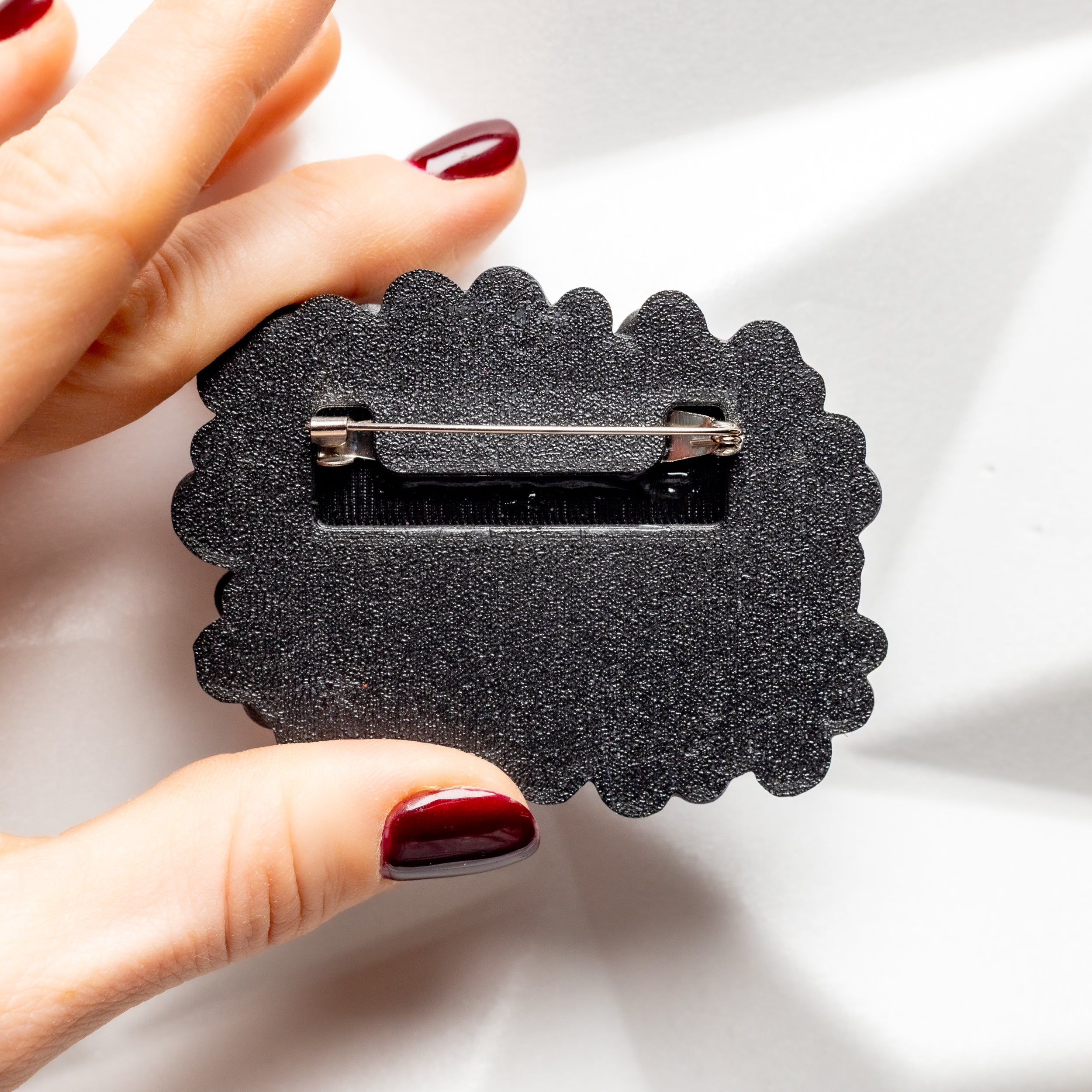 Black textured brooch back held by a hand on a light background