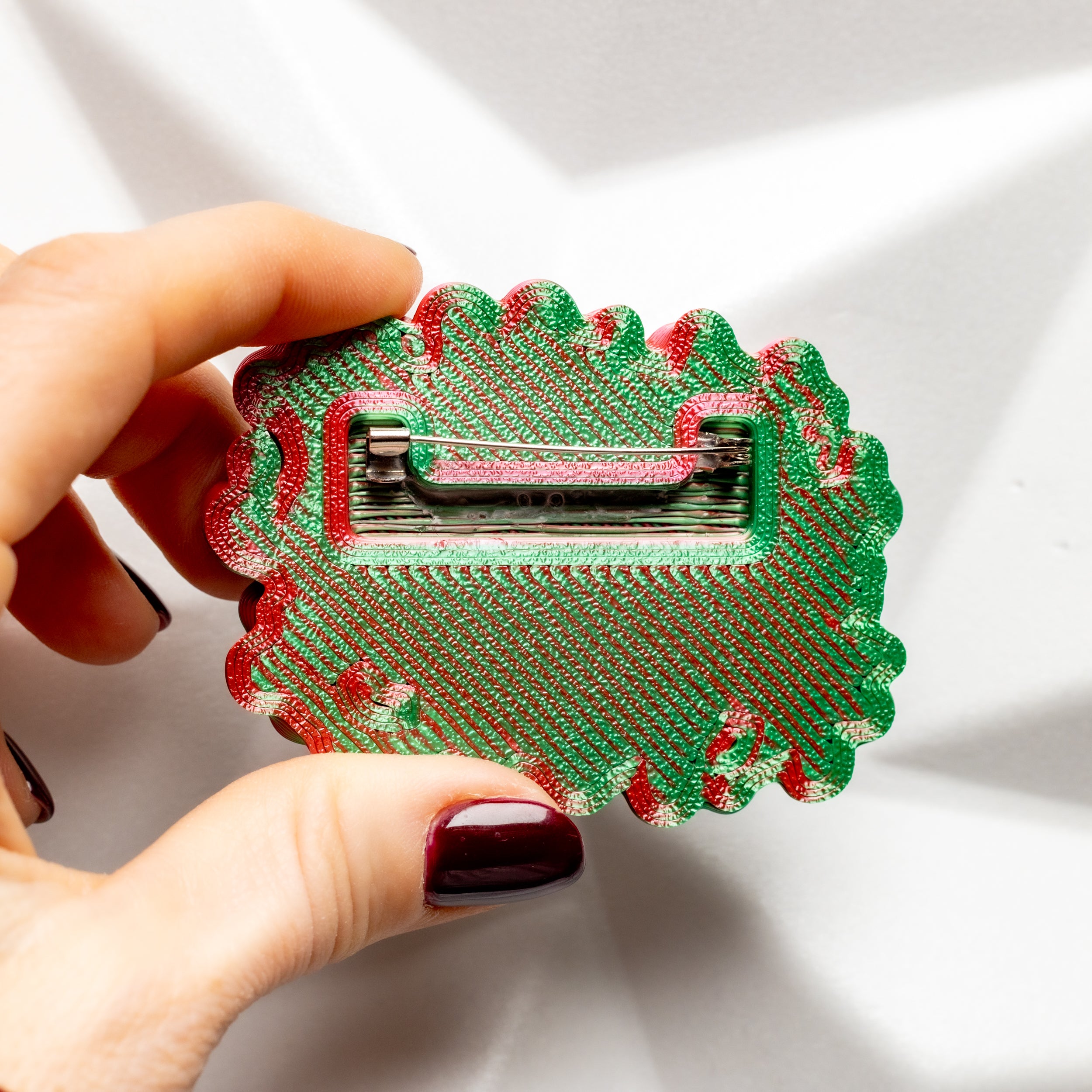  a decorative brooch with red and green pattern on a white background