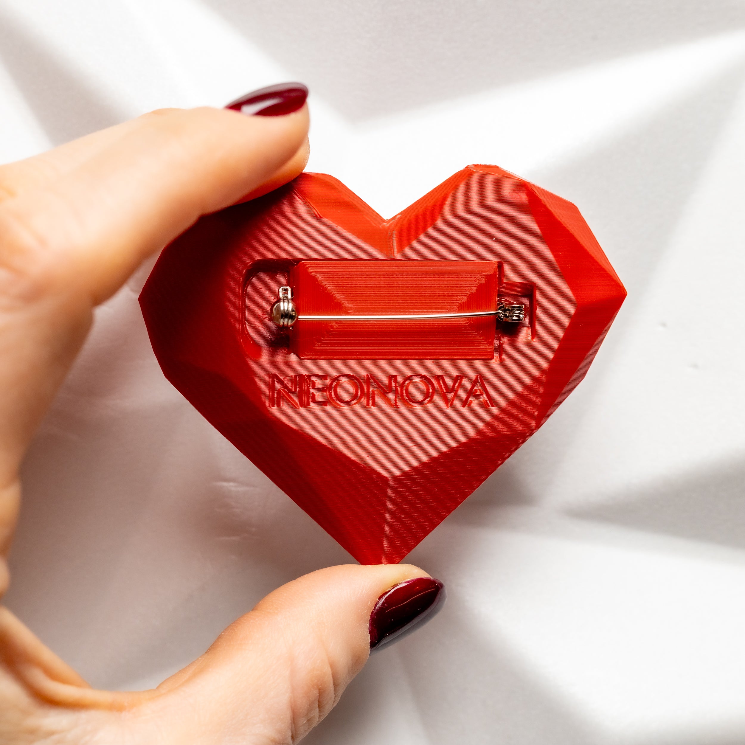 Red heart-shaped object with 'NEONOVA' branding held by a hand on a white background