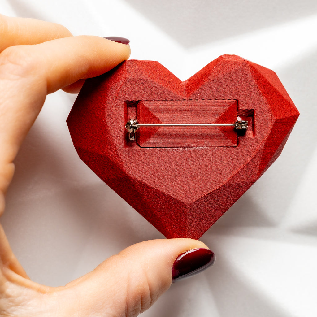 Red heart-shaped brooch held by a hand on a white background