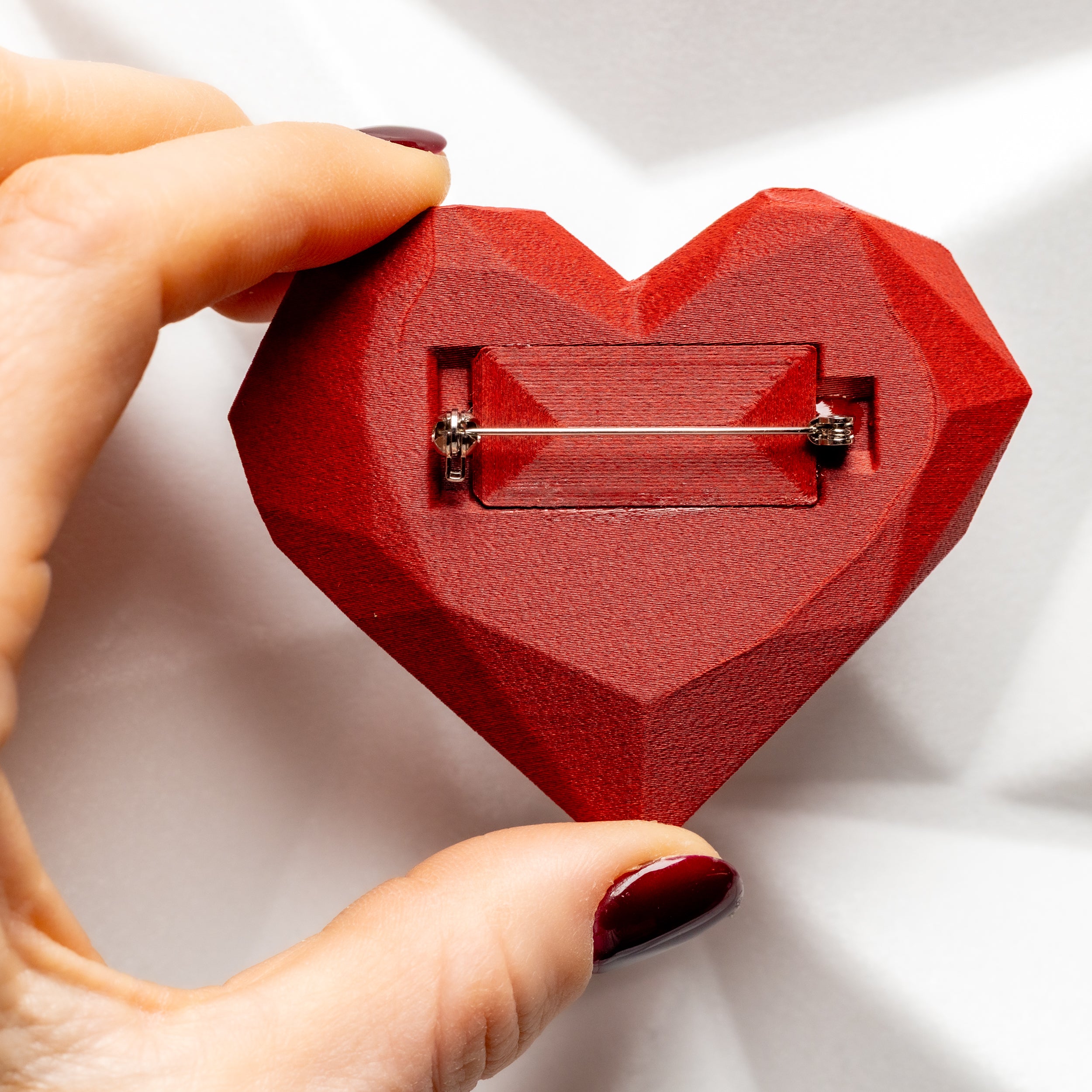 Red heart-shaped brooch held by a hand on a white background