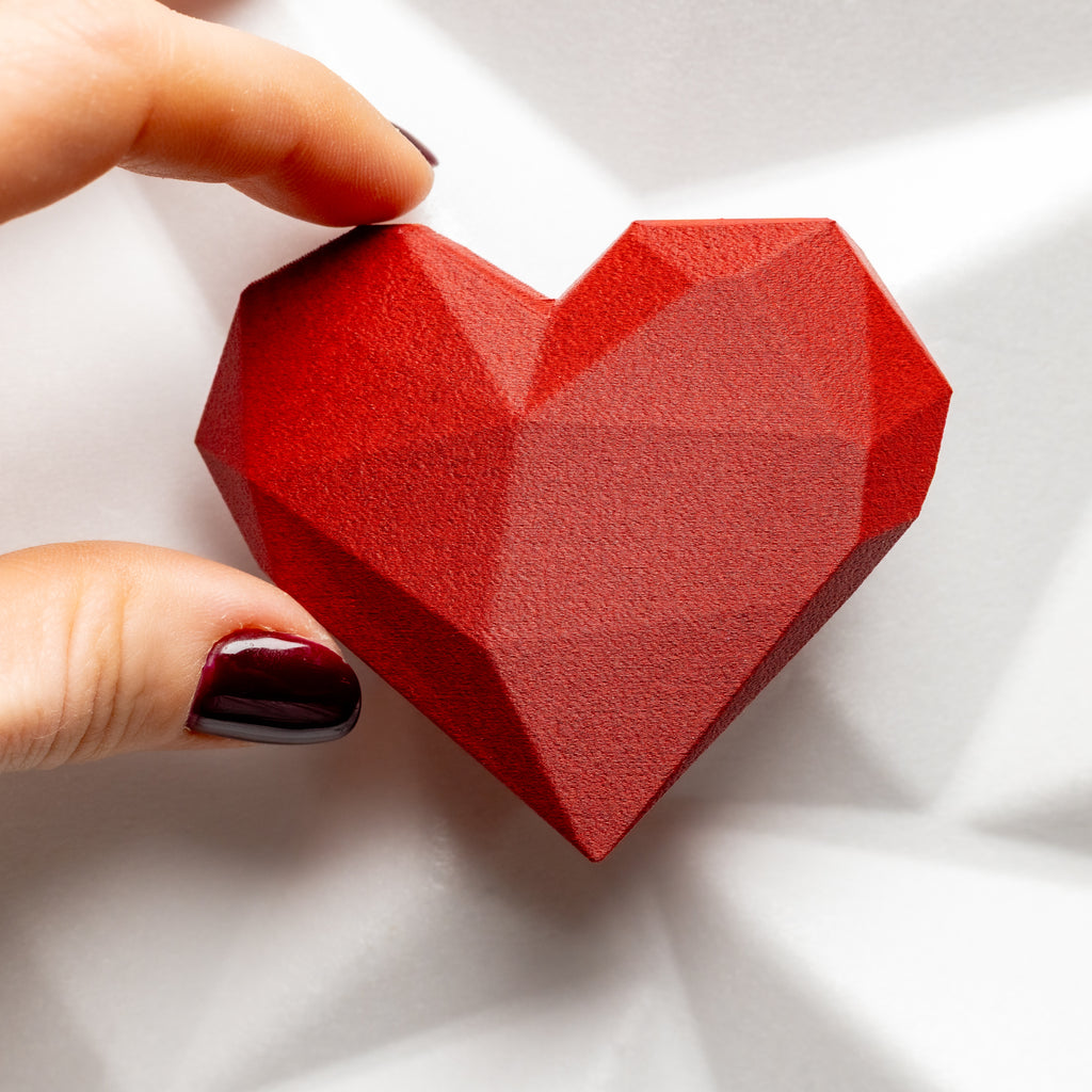 Red  matte geometric heart held by a hand on a white background