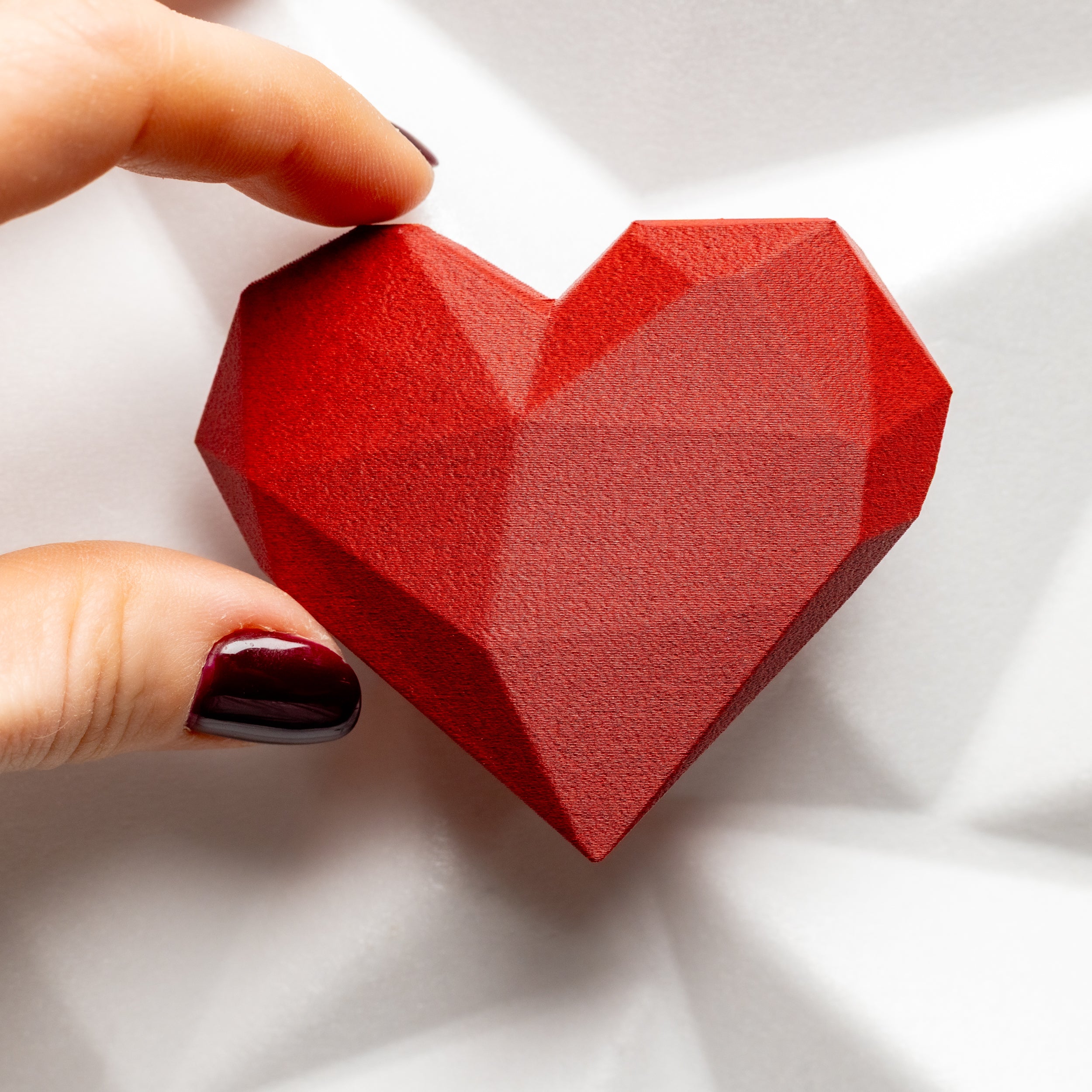 Red  matte geometric heart held by a hand on a white background