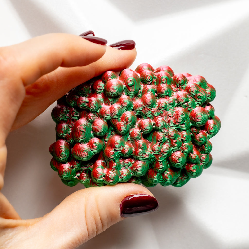 Hand holding a red and green textured brooch against a white background